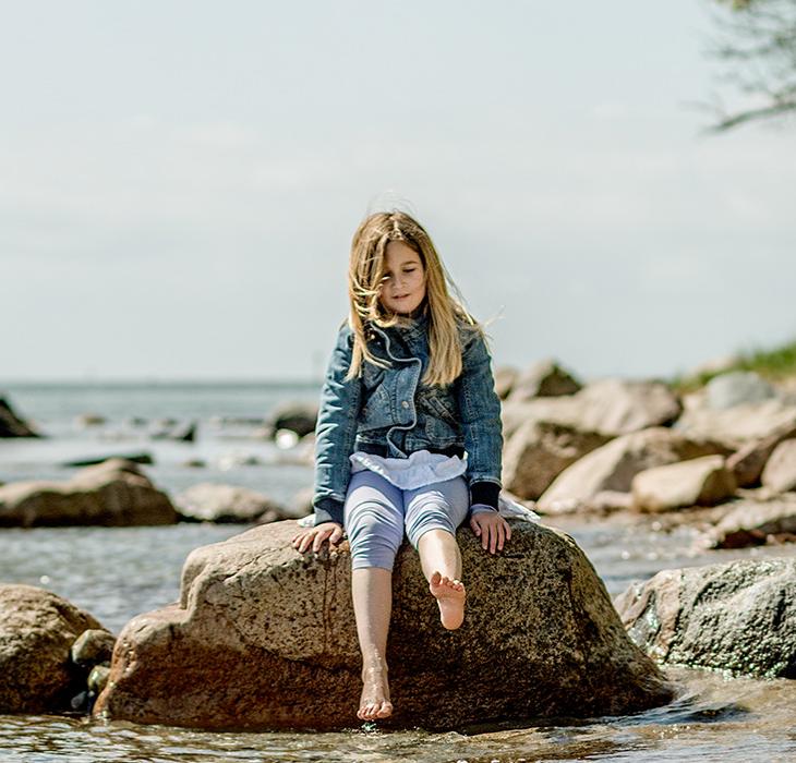 Pige sidder på sten i strandkanten